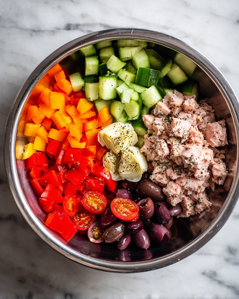 A large metal bowl contains several layers of fresh ingredients arranged side by side: bright green diced cucumber at the top left, small orange bell pepper cubes at the top right, and halved red cherry tomatoes with seeds showing at the bottom right. Next to the tomatoes is a pile of chunky light pink tuna mixed with some black pepper sprinkled on top. Below the tuna, there are dark purple sliced olives. On the left side, there are red diced bell peppers, and in the center, there is a small mound of pale artichoke hearts with a drizzle of oil and a sprinkle of black pepper. The bowl sits on a white marbled surface. photo taken with an iphone --ar 4:5 --v 7