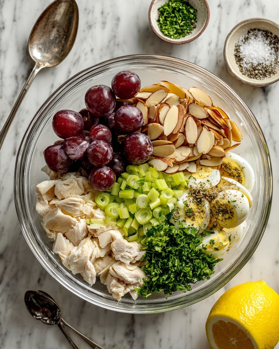 A clear glass bowl shows seven layers of ingredients arranged side by side, starting with dark red halved grapes on the top left, next to light brown sliced almonds on the top right, then bright green sliced scallions below the almonds, followed by small white chicken pieces on the bottom right. In the middle near the chicken are light cream-colored mayonnaise and yellow mustard with some black pepper on top. On the bottom left side are light green celery pieces and finely chopped dark green parsley beside them. The bowl sits on a white marbled surface next to a silver spoon and a small bowl of salt and pepper above it, and a lemon half at the bottom left. photo taken with an iphone --ar 4:5 --v 7