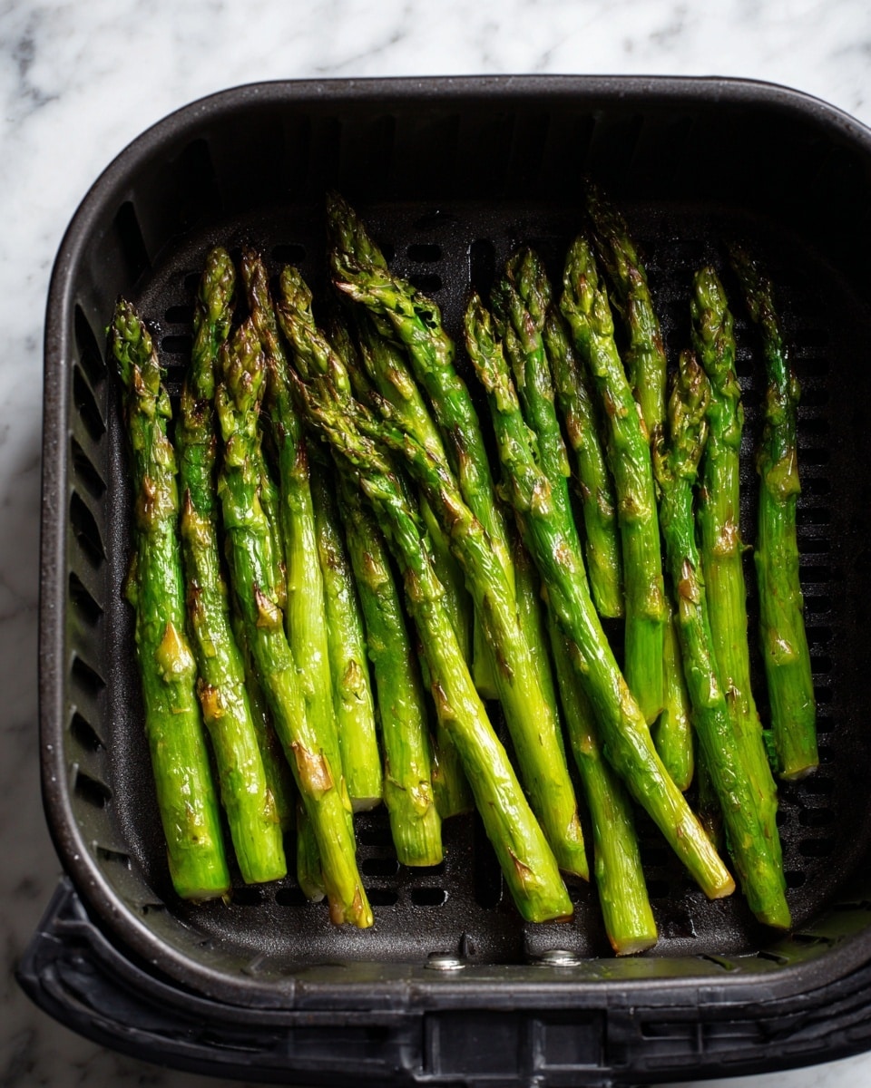 A white plate holds a neat pile of bright green asparagus stalks arranged side by side, cooked to a light char with some brown spots. On top of the asparagus is a sprinkle of finely shredded white cheese, adding texture and contrast. There are three lemon wedges placed around the asparagus on the plate, two on one side and one on the other. Small cracks of black pepper are scattered around the plate, and the plate sits on a white marbled surface. Photo taken with an iphone --ar 4:5 --v 7