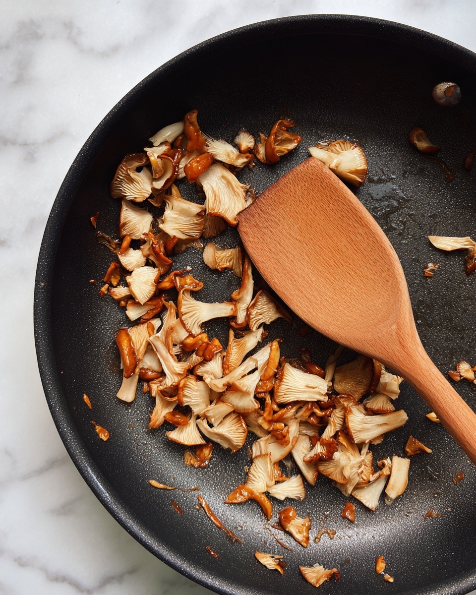 A black frying pan with a slightly worn and shiny surface holds many small, cooked mushroom pieces scattered around, showing light brown and beige colors with some darker caramelized spots. A wooden spoon with a smooth texture rests on top of the mushrooms, positioned diagonally from the bottom right to the center. The background is a white marbled texture. photo taken with an iphone --ar 4:5 --v 7